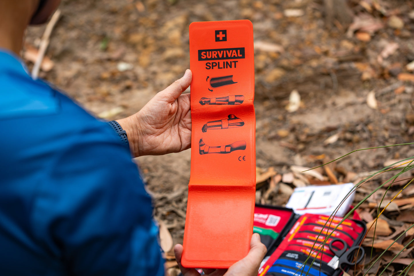 Person holding the orange SURVIVAL splint beside the opened Slimline kit