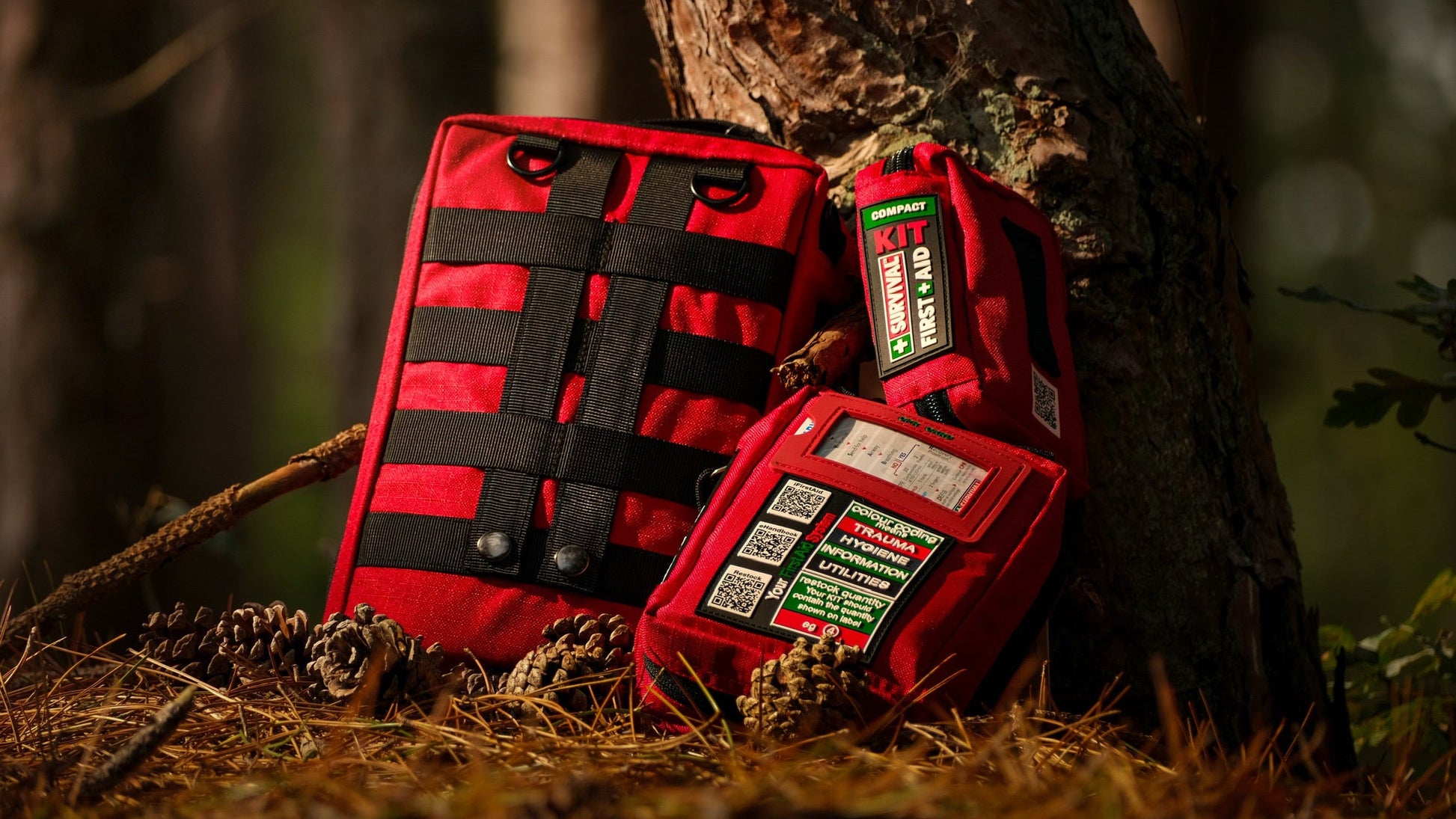 Two red SURVIVAL first aid cases outdoors against a tree trunk