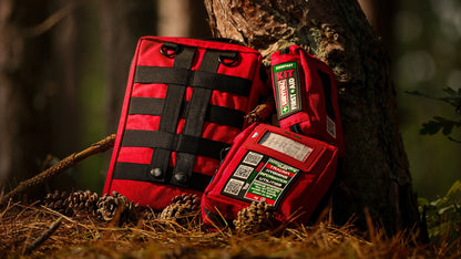 Two red SURVIVAL first aid cases outdoors against a tree trunk