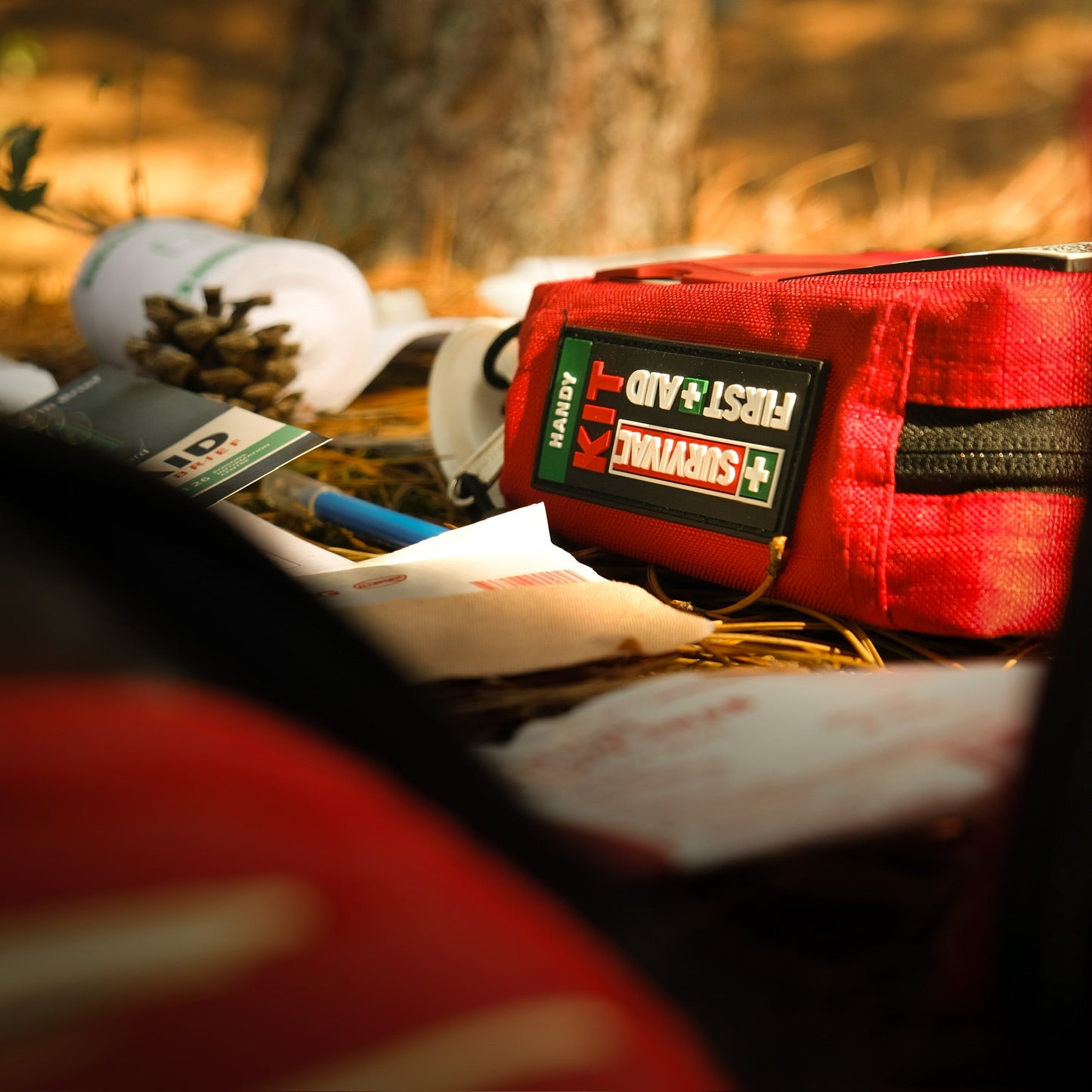 Red SURVIVAL first aid case on the ground beside a fallen tree