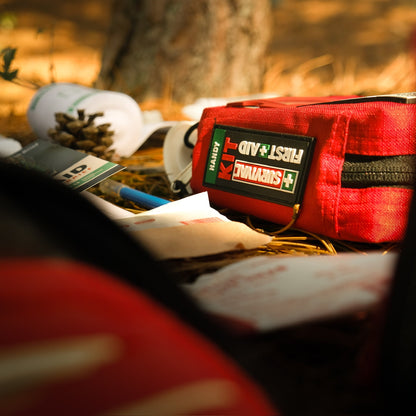 Red SURVIVAL first aid case on the ground beside a fallen tree
