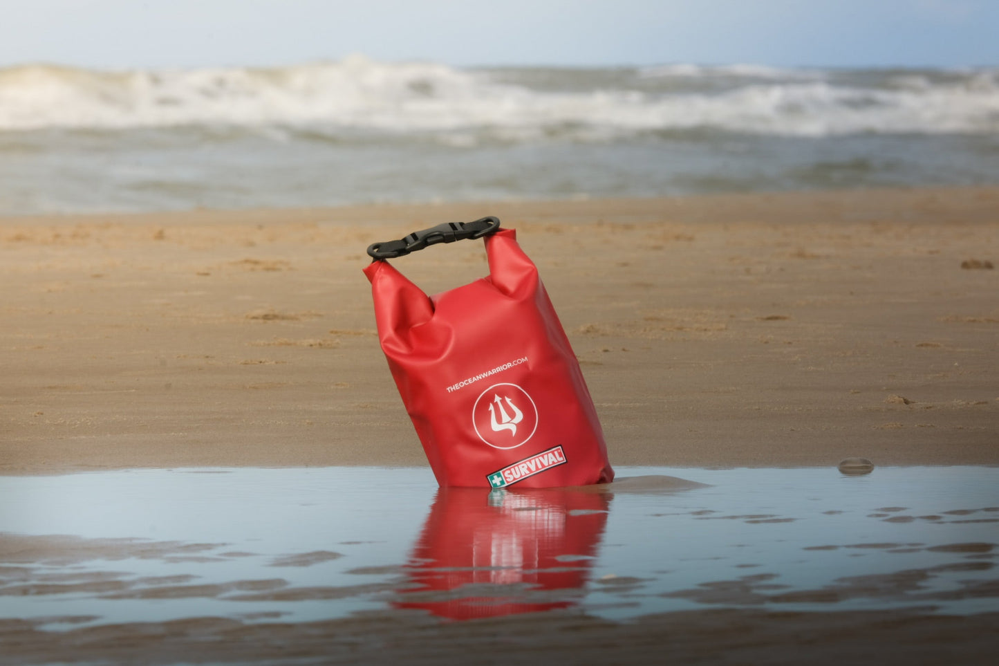 Red dry bag floating upright in shallow water at the beach