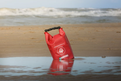 Red dry bag floating upright in shallow water at the beach